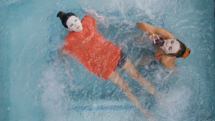 Yüz maskeli iki genç kız havuzda yüzüyor